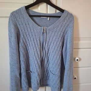 Ljusblå stickad kofta med dragkedja - Säljer en ljusblå stickad kofta med snyggt strukturerat mönster och praktisk dragkedja framtill. Köpt second hand passar M/L