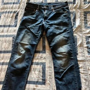 Levi's 502 mörkblå jeans - Säljer ett par Levi's 502 jeans i mörkblå tvätt med klassisk femficksdesign och snygga slitningar framtill. Jeansen har rak passform och normal midja, med Levi's ikoniska röda etikett och läderpatch bak. Perfekt för dig som gillar tidlös streetstil.
