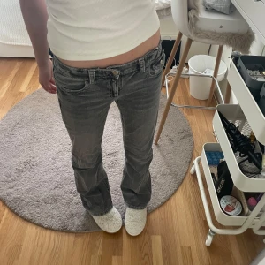 Grå bootcut jeans - ginatricot  - Säljer ett par grå jeans med bootcut passform och låg midja. Jeansen har snygga broderade detaljer på bakfickorna och slitna kanter för en cool vibe. Materialet är klassisk jeans och färgen är mörkgrå med tvättad look. 