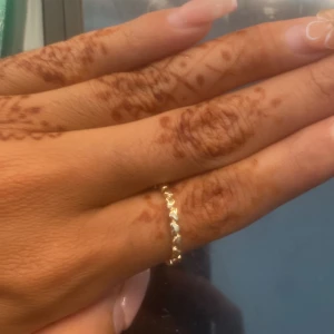 Set med tre tunna guldringar - Säljer ett set med tre stilrena guldfärgade ringar. En ring har en rund klar sten, en är enkel och vågig, och den tredje har ett mönstrat band med små detaljer runt hela ringen. Perfekt för dig som gillar att mixa och matcha smycken och vill ha en clean look.