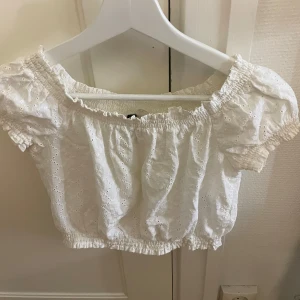 Vit broderad bolerotopp från H&M - Superfin vit bolerotopp från H&M med broderade detaljer och puffiga korta ärmar. Toppen har smock vid halsringning, ärmslut och nederkant för en söt och trendig look. Perfekt för sommarens alla häng och selfies!