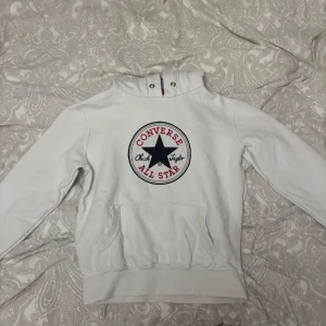 Vintage hoodie från converse - Säljer en vit hoodie från Converse med stor All Star-logga på bröstet i svart och rött. Tröjan har huva med grått foder, känguruficka och långa ärmar. Perfekt för chill dagar och streetstyle. Klassisk och enkel design som funkar till det mesta. Storleken säger L men skulle säga att det är typ S eller M. Tröjan är jätteskön, och märket på armen är inte alls synligt, tror även man kan få bort det.