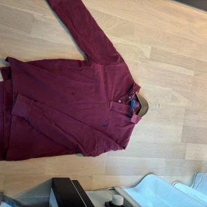 Vinröd pikétröja från Polo Ralph Lauren - Säljer en vinröd långärmad pikétröja från Polo Ralph Lauren, modell Custom Slim Fit.  Storlek m men sitter som S. Tröjan har klassisk krage, två knappar vid halsen och den ikoniska blå logon broderad på bröstet. Materialet är mjuk bomull som känns skön mot huden. Kvitto finns