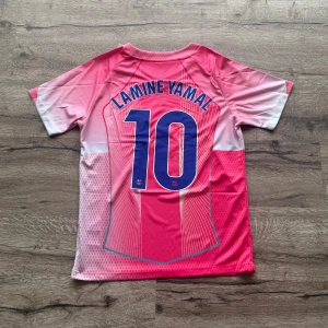 Barcelona Lamine Yamal #10 rosa matchtröja - Snygg Barcelona fotbollströja med Lamine Yamal och nummer 10 på ryggen. Tröjan är rosa med vita och blå detaljer, har korta ärmar och coola grafiska linjer. Nike-logga, Spotify-sponsor och Barca-emblem på bröstet. Perfekt för dig som vill sticka ut på planen. Storlek: S helt ny med prislapp. Priset är inte hugget i sten så skicka pm vid funderingar 