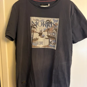 Morris t shirt - Snygg mörkblå t-shirt från Morris i bomull, med coolt tryck framtill som visar palmer och båtar i beige, blått och brunt. Klassisk rund hals och korta ärmar. Perfekt för dig som gillar stilrena plagg med lite extra detaljer.