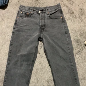 Levi's 501 mörkgrå jeans straight fit - Säljer ett par Levi's 501 jeans i mörkgrå tvätt med klassisk straight fit. Jeansen har fem fickor, knappgylf och den ikoniska läderpatchen bak. Materialet är slitstarkt denim och passformen är normal. Perfekt för dig som gillar tidlös stil och vill ha ett par schyssta jeans.