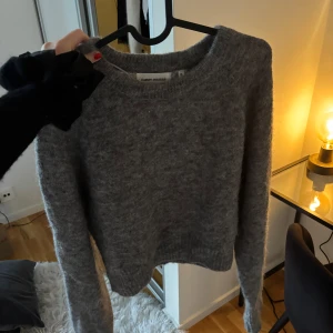 Grå stickad tröja Carin Wester - Mysig grå stickad tröja från Carin Wester i storlek XS. Tröjan har rund halsringning och långa ärmar, perfekt för kyliga dagar. Den är fluffig och har en enkel, klassisk design som är lätt att matcha med jeans eller kjol.