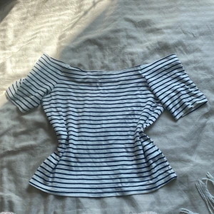 Randig offshoulder topp  - Säljer en vit och svart randig offshoulder topp med korta ärmar. Toppens passform är lös och den är gjord i viskos. Perfekt för dig som gillar en chill och stilren vibe med lite fransk känsla. Enda nackdelen är att det finns tre små fläckar, jag vet inte om det går bort när man tvättar men skulle tro det ❣️🥰 strorlek M men passar mer som S eller XS