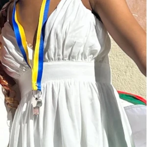 Vit omlottklänning med volang - Supersöt vit kortklänning med omlott upptill och bred midja. Klänningen har tunna axelband, v-ringad hals och volangdetaljer på kjolen. Materialet är mjukt och luftigt, perfekt för varma dagar. Stilren och fräsch look som är lätt att matcha med accessoarer.