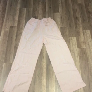 Ljusrosa linnebyxor från Grunt XL - Säljer ett par ljusrosa linnebyxor från Grunt i storlek XL. Byxorna har en loose passform, breda ben och elastisk midja med snörning för extra komfort. Perfekta för chill dagar och sommarhäng. Materialet är lätt och luftigt linne.