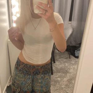 Blommig långkjol i blå och gröna toner - Säljer en flowy långkjol med blommigt och paisleyinspirerat mönster i blå, gröna och orangea nyanser. Kjolen har bred resår i midjan och är gjord i ett lätt, mjukt material. 