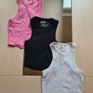 3-pack ribbade linne-toppar XXS FSBN Sister - Tre ribbade linne-toppar från FSBN Sister i storlek XXS. Färgerna är rosa, svart och vit. Alla har klassisk ärmlös design med rund halsringning och tight passform. Perfekta att matcha med jeans eller shorts för en chill look. Alla förutom den vita har inga defekter, vita har dock lite fläckar. Säljer även dem separat!