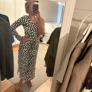 Prickig långklänning med slits - Säljer en vit långklänning med svarta prickar och oneshoulder-design. Klänningen har lång ärm på ena sidan och en snygg slits längs benet. Materialet känns lätt och flowy. Det är verkligen det snyggaste i min garderob men den går tyvärr inte över bysten (har 75D). Jag köpte den från Sellpy för 550kr och har aldrig användt den själv, men som man ser på bilderna så finns det några defekter och innetyget är bortklippt, det påverkar dock inte hur den ser ut på 🩷🙏🏻Helt slut fr. mango, nypris ca1200