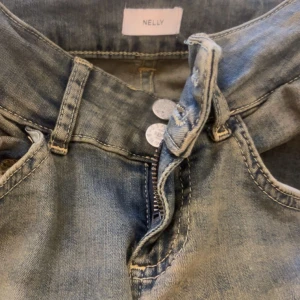 Blå jeans från Nelly med fickdetalj - Snygga blå jeans från Nelly med klassisk femficksdesign och en extra ficka med lock bak. Jeansen har dragkedja och dubbla knappar framtill. Perfekta för dig som gillar en enkel men cool look.