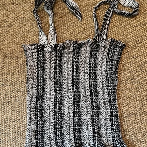 Svartvit smockad linnetopp med knytband - Supersöt smockad linnetopp i svart och vitt med knytbara axelband. Toppen har ett mixat mönster med ränder och prickar, och är croppad med en stretchig passform. Perfekt för att ge din outfit en cool och lekfull vibe.