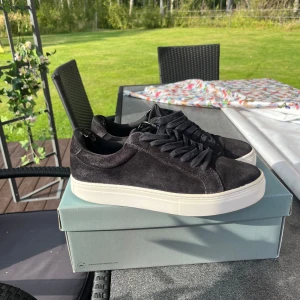 Svarta sneakers från Vagabond i mocka - Stilrena svarta sneakers från Vagabond med ovandel i mjuk mocka och klassisk vit platt sula. Skorna har rund tå, svarta skosnören och en clean look som passar till det mesta. Perfekta för dig som gillar minimalistisk och modern stil.