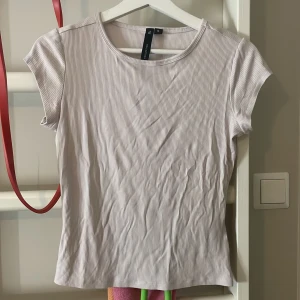 Ljusribbad topp från Lager 157 - Supersnygg ljus ribbad topp från Lager 157. Modellen har korta ärmar, rund halsringning och en slim passform. Perfekt att styla med jeans eller kjol för en clean look.