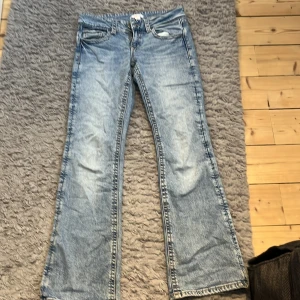 Ljusblå bootcut jeans med fickdetaljer - Snygga ljusblå jeans med bootcut passform och coola fickdetaljer bak med knappar. Jeansen har klassisk femficksdesign och lätt tvättad look. Perfekta för dig som gillar en avslappnad men trendig stil.