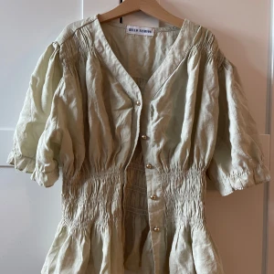 Ljus grön kofta från Hello Fashion - Supersöt ljus grön kofta från Hello Fashion med puffiga korta ärmar, v-ringning och snygga guldfärgade knappar framtill. Klänningen har smockad midja och volang nedtill, vilket ger en chill och trendig siluett. Perfekt för dig som gillar en luftig och stilren look.