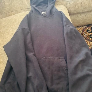 Svart hoodie från YOURTURN i storlek L - Svart hoodie från YOURTURN i storlek L. Klassisk modell med huva och stor magficka framtill. Mjuk insida och skön passform, perfekt för chill eller häng. Materialet är bomull och polyester, vilket gör den både bekväm och slitstark. Snyggt diskret logotypmärke på sidan.