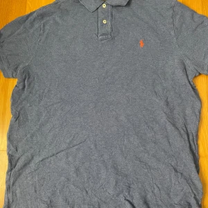 Blå Polo Ralph Lauren t-shirt XL - Snygg blå t-shirt från Polo Ralph Lauren i custom slim fit. Klassisk pikékrage med två knappar och den ikoniska broderade loggan på bröstet. 