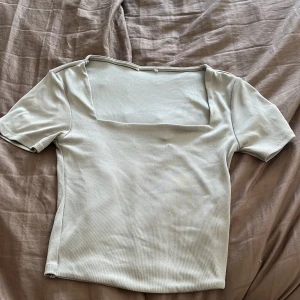 Ljusgrå ribbad topp med fyrkantig ringning - Ljusgrå topp med ribbad struktur och fyrkantig ringning. Kortärmad och figurnära passform. Använd få gånger men är lite knottrig på framsidan