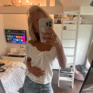 Vit offshoulder blus med rosett😇 - Superfin vit blus med offshoulder och korta puffärmar. Blusen har broderade hålmönster och en söt rosett framtill. Perfekt till jeans eller kjol för en fräsch sommarlook. Luftig och lätt i bomullsmaterial. 