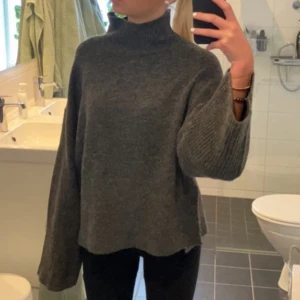 Mörkgrå  polotröja - Säljer en mörkgrå, oversized polotröja med breda, långa ärmar och hög krage. Tröjan är stickad och har en loose passform som ger en chill och avslappnad vibe. Perfekt för kalla dagar när du vill vara både bekväm och snygg.