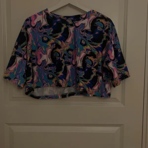 Crop top - Färgglad crop top från SHEIN med psykedeliskt mönster i blått, rosa och gult. Perfekt för sommaren – bär den till shorts, kjol eller över ett linne. Lätt och bekväm, passar både strand, festival och vardag. Stick ut med en unik och lekfull stil!
