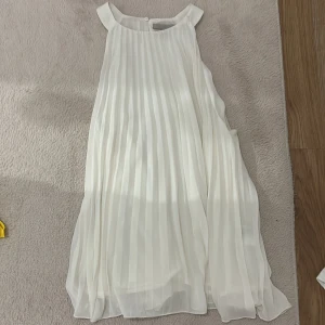 Vitt plisserat halterneck linne - Supersöt vit topp från H&M med plisserad design och ärmlös modell. Toppen har rund halsringning och knäppning bak i nacken. Luftigt tyg som ger ett flowy och elegant intryck, perfekt för varma dagar, fester eller firanden