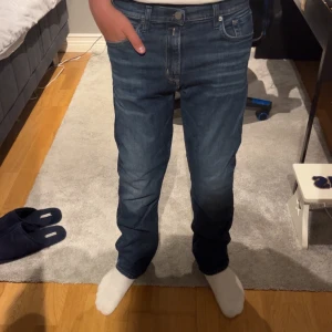 Blå jeans från Replay, modell Thad - Snygga blå jeans från Replay i modellen Thad. Replay-logga på fickan och silverfärgad knapp. Jeansen har en rak passform och är tillverkade i slitstarkt denim med coola ljusa tvätteffekter. Perfekt för dig som gillar stilrena och tidlösa jeans. Passar mig som är 175 cm och sitter lite stort pga modellen. Skit snygga till allt🤩