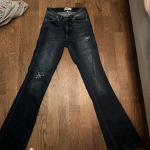 Bootcut jeans från ONLY, mörkblå - Mörkblå bootcut jeans från ONLY med slitna detaljer på låret och knät, skulle säga att dom är mid Waist så inte lowwaist🥰är inte så använda. Har gjort hålen själv.