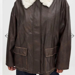 Brun PU jacka med mjuk fuskpälsmaterial på insidan - Säljer en brun PU jacka från NA-KD med oversized passform. Jackan har stora fickor framtill, dragkedja och är fodrad med mjuk fuskpälsmaterial på insidan. Perfekt för kalla dagar och ger en cool vintage vibe.