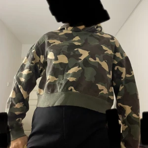 Camouflage mag-hoodie  - Säljer en magtröja hoodie från H&M Divided i storlek M. Tröjan har ett klassiskt camouflage-mönster i grönt, beige och brunt, med huva och bred mudd nertill. 