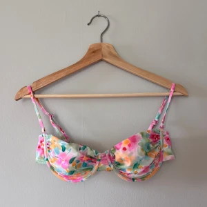 Blommig bikiniöverdel i pastellfärger - Superfin bikiniöverdel med blommigt mönster i pastelliga nyanser av rosa, grön, gul och orange. Balconette-modell med bygel och justerbara axelband. I storlek S, säljes pga. passar inte mig längre. Använd få gånger. Köpt för 259 kr.