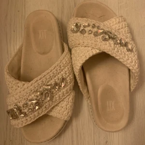 Beige sandaler med pärldetaljer från dina sko  - Snygga beige sandaler från din sko med breda, virkade band i bomull och stora glittrande pärldetaljer på ovansidan. Platt sula och öppen tå gör dem perfekta för varma dagar. Ger en chill men ändå glam känsla till din outfit. Inte använt alls mycket för dom är för stora för mig. 