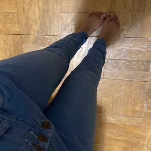 Blå jeansbyxor från Moods Jeans - Snygga blå jeansbyxor från Moods Jeans med hög midja och flera knappar framtill. Byxorna har en slim passform och är perfekta för en stilren look. De är tillverkade i ett bekvämt denimtyg som ger en skön känsla hela dagen.