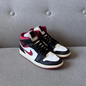 Nike Air Jordans i svart, vitt och rött - Snygga Nike Air Jordans i klassisk färgkombination av svart, vitt och rött. Skorna har en hög modell med snörning och en ikonisk Nike-logga på sidan. Perfekta för dig som vill ha en stilren och sportig look.