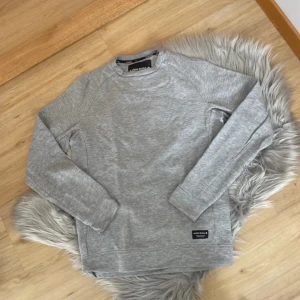 Grå tröja från Björn Borg - Säljer en stilren grå tröja från Björn Borg. Tröjan har en klassisk design med rund hals och långa ärmar. Perfekt för en avslappnad look. Märkeslogga syns diskret på framsidan.