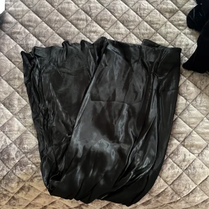 Svart långkjol i satin - Elegant svart långkjol i satin med en glansig finish. Perfekt för en stilren look. Kjolen har en flytande passform som ger en vacker siluett.