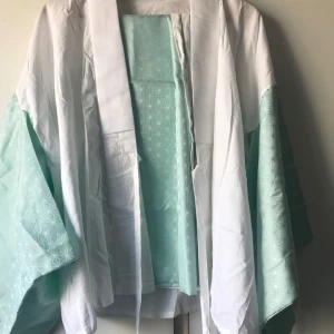 Vit och mintgrön kimono - Säljer en elegant kimono i vitt och mintgrönt med ett subtilt geometriskt mönster. Den har vida ärmar och en öppen front med knytband. Perfekt för en stilfull look.