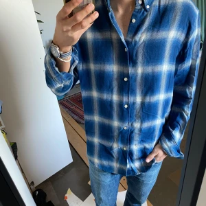Blå rutig skjorta - Snygg blå rutig skjorta med vita rutor och knappar. Skjortan har en klassisk krage och långa ärmar, perfekt för en avslappnad stil. Passar bra till jeans eller chinos.