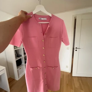 Rosa klänning från Zara - Säljer en rosa klänning från Zara med korta ärmar och guldknappar framtill. Figursydd modell och virkat tyg! Använd 1 gång