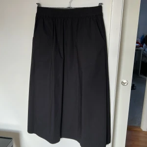 Svart långkjol från Gerry Weber - Säljer en stilren svart långkjol från CC Heart (danskt) i bomull/poplin. Kjolen har en elastisk midja för extra komfort och en klassisk design med två fickor i sidorna. Perfekt för dig som vill ha en cool, tidlös och mångsidig kjol till vardags.