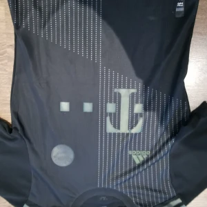 Svart fotbollströja från Adidas - Säljer en svart fotbollströja från Adidas med ett stilrent mönster och en diskret logga. Tröjan har korta ärmar och en modern design. Perfekt för fotbollsfans som vill ha något unikt och snyggt. (Logan bakom tröjan är sliten) 