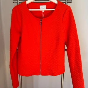 Ny, oanvänd, röd orange jacka från Vila!  - Ny, oanvänd, röd orange jacka från Vila i storlek M med prislappen kvar. Jackan har ett fint mönster i tyget och passar perfekt nu till våren. Nypris 350kr