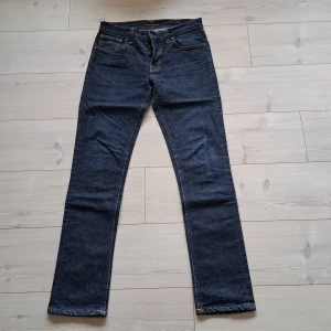 Mörkblå jeans från Nudie - Snygga mörkblå jeans från Nudie med klassisk femficksdesign och orange sömmar. De har en knappgylf och en läderpatch med logotyp baktill. Perfekta för en stilren look.