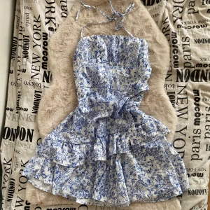 Blåvit blommig klänning - Charmig blåvit klänning med blommigt mönster och volanger. Perfekt för sommarn.