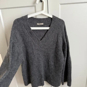 Grå stickad tröja med v-ringning - Säljer en mysig grå stickad tröja med v-ringning. Perfekt för kyliga dagar med sin mjuka och bekväma passform. Tröjan har långa ärmar och ribbade kanter som ger en stilren look. Tröjan är använd fåtal gånger men inga skavanker. Jätteskön att ha på sig och skön till sommarkvällar. 