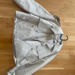 Beige trenchcoat med knappar - Säljer en stilren beige trenchcoat med knappar och klassisk krage. Aldrig använd. Prislapp kvar. OBS: står XS men är superstor i storleken så passar en M-L. Säljes pga av för stor. 
